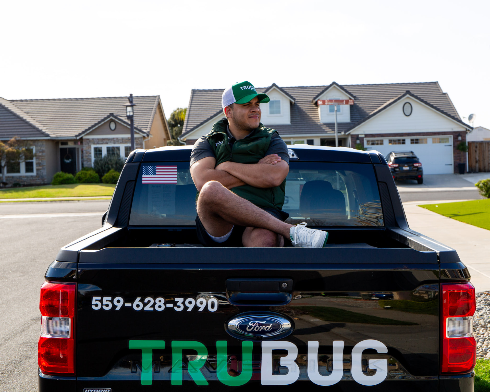 TruBug technician sitting on the tailgate of a black branded truck