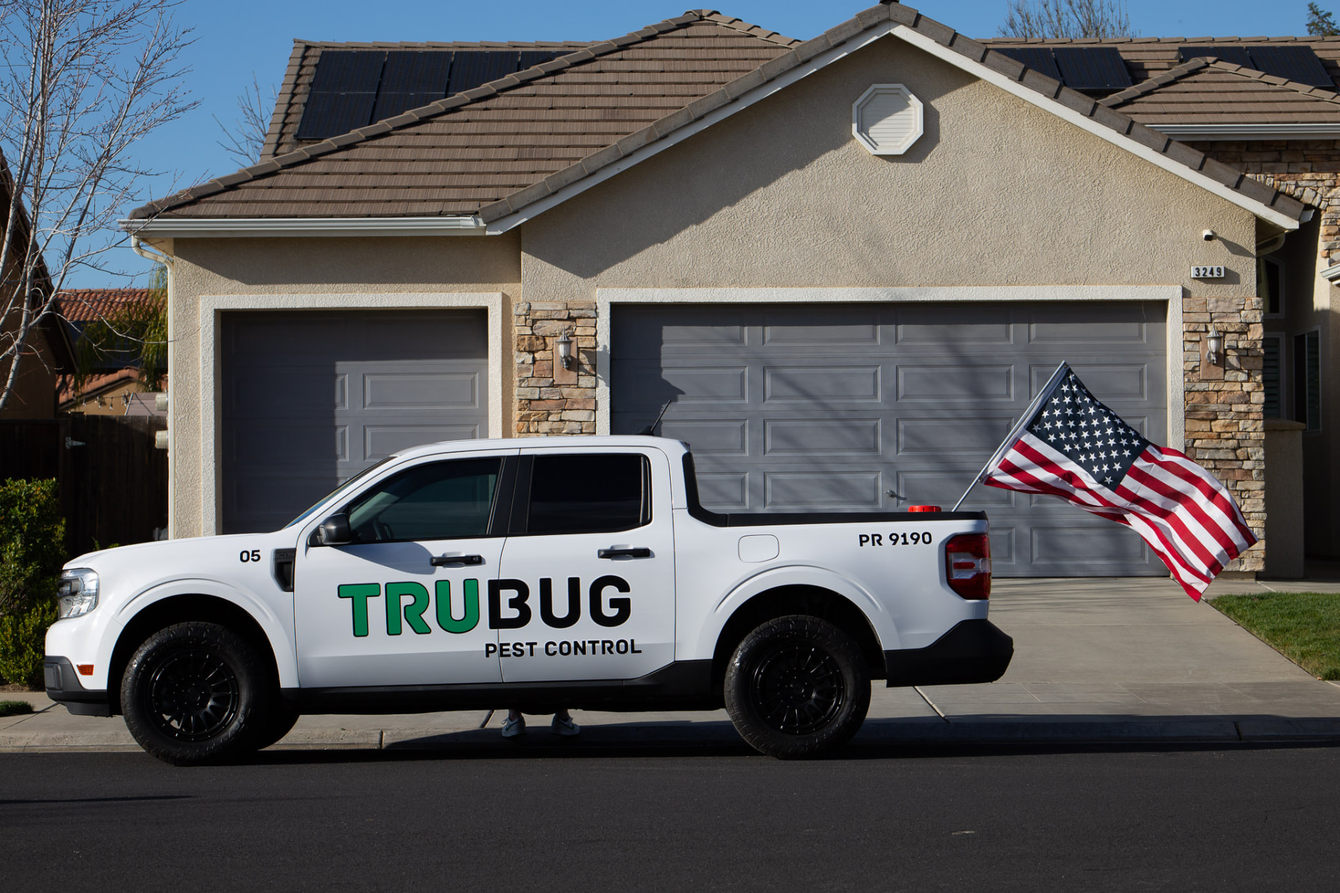 White TruBug Pest Control truck with an American flag parked in a driveway