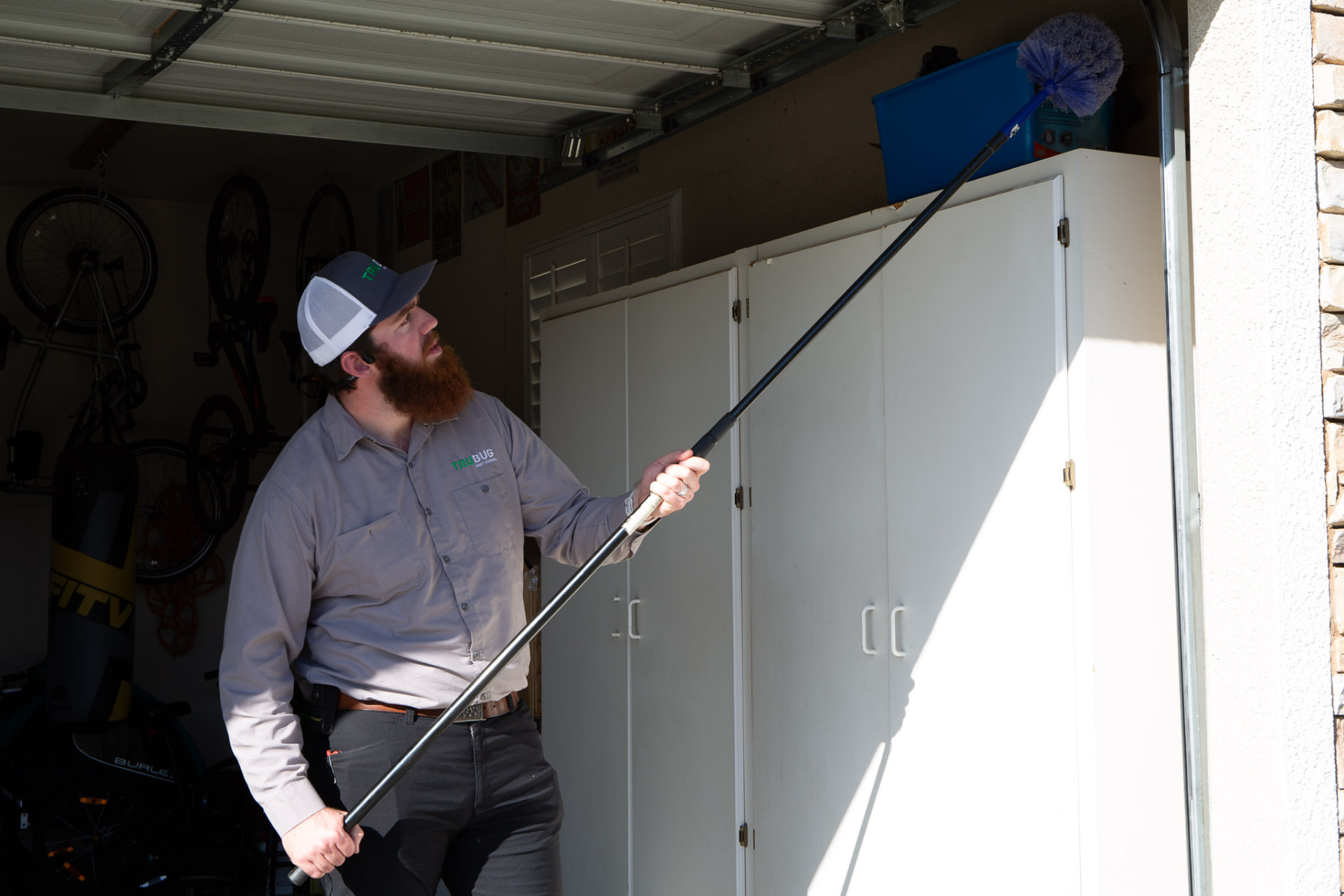 TruBug technician de-webbing a garage ceiling with an extension duster