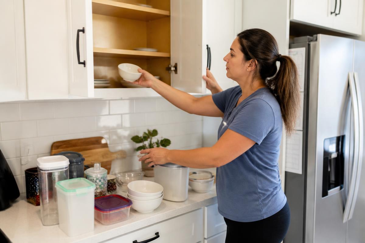 Homeowner clearing kitchen cabinet contents onto the counter before a roach treatment